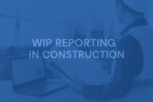 Construction manager in a hard hat reviewing project documents next to a laptop on a job site, representing how WIP reporting in construction helps track costs, project progress, billing, and profit margins.